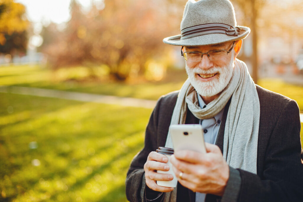 an older man looking at his cell phone in a park making progress towards discovering his dream business in a committed community